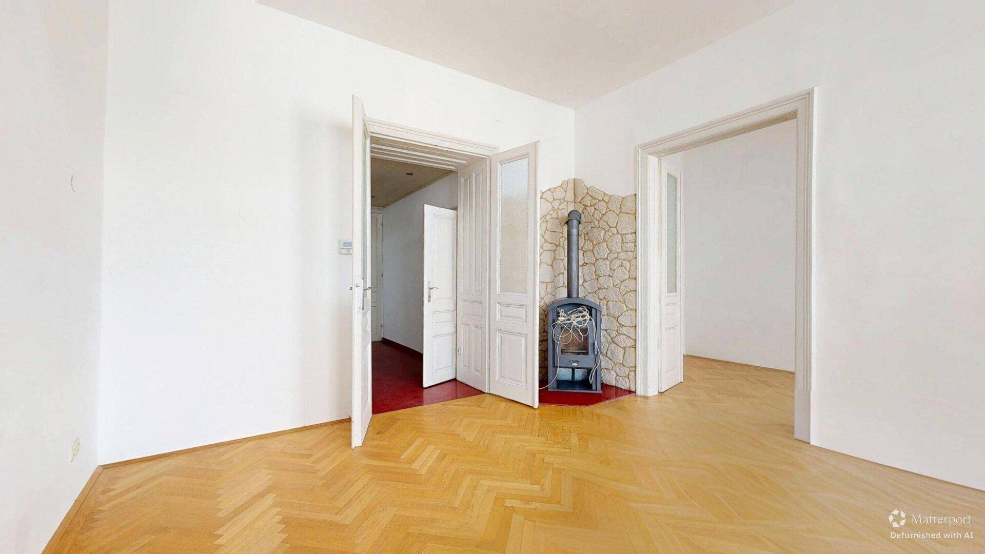 Geräumiges Zimmer mit Fischgrätparkett und einem modernen Holzofen vor einer Steinwand.