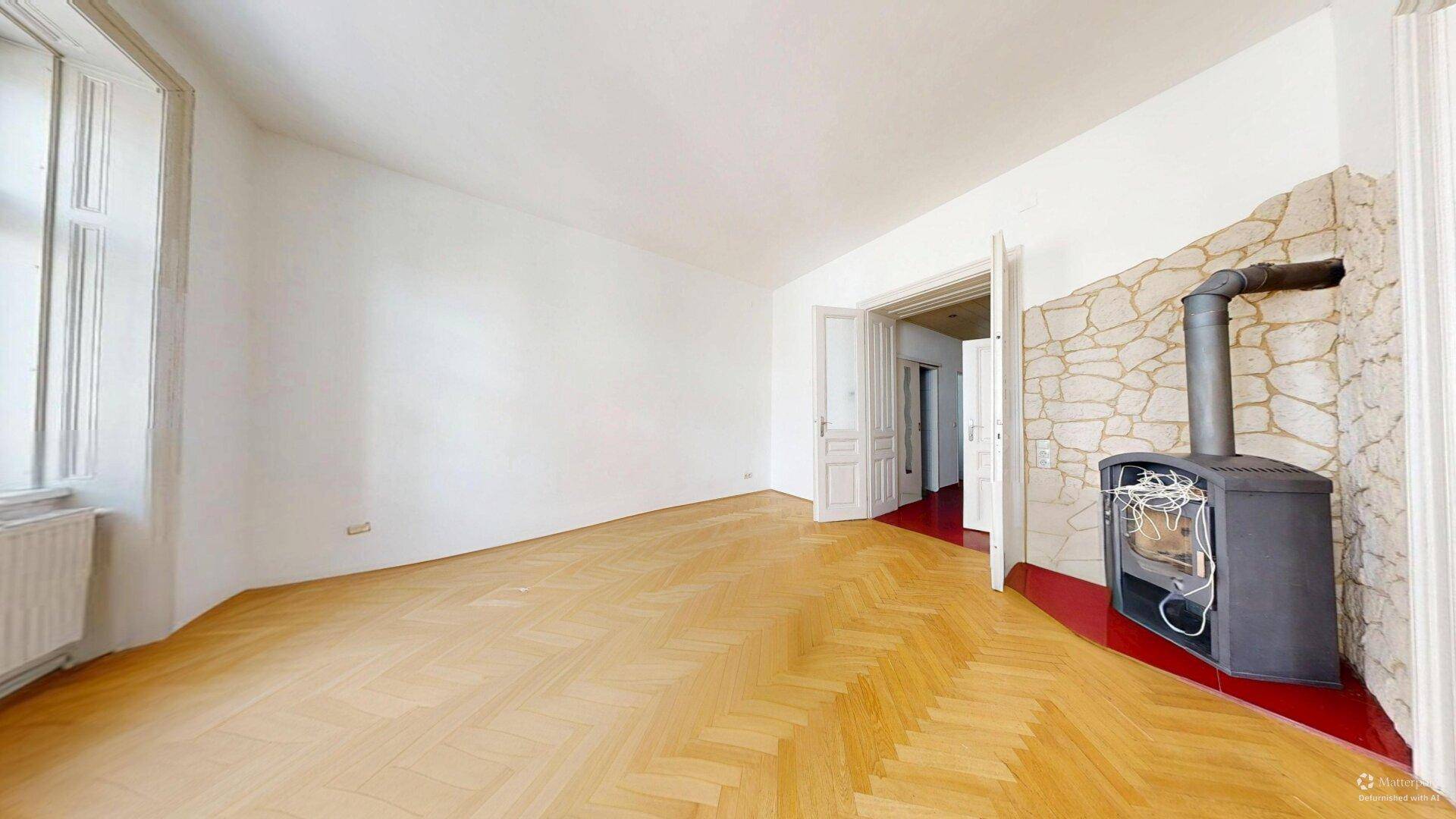Helles Zimmer mit Fischgrätparkett und einem modernen Holzofen vor einer Steinwand.