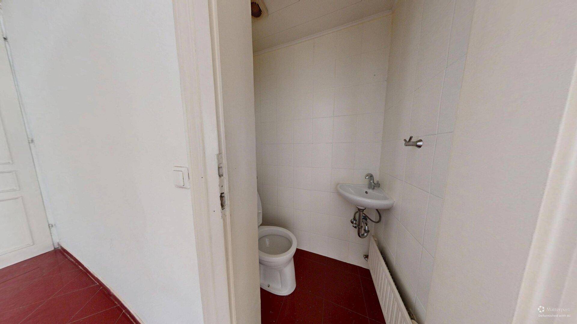 Separates WC mit Toilette, kleinem Waschbecken und roten Bodenfliesen.