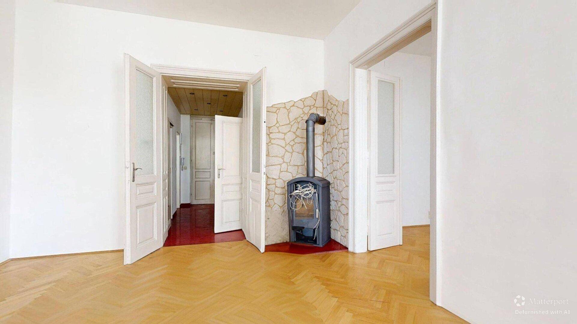 Geräumiges Zimmer mit Fischgrätparkett, Holzofen und mehreren Türen zu angrenzenden Räumen.