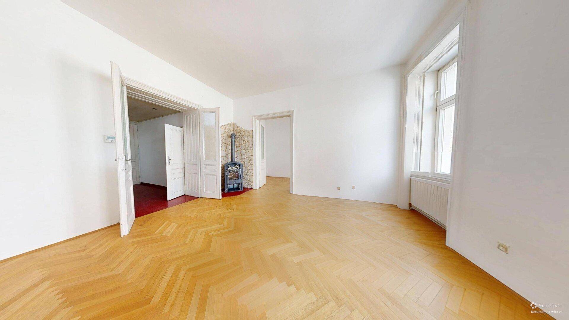 Großes, helles Zimmer mit Fischgrätparkett und einem Holzofen, ideal für gemütliche Abende.