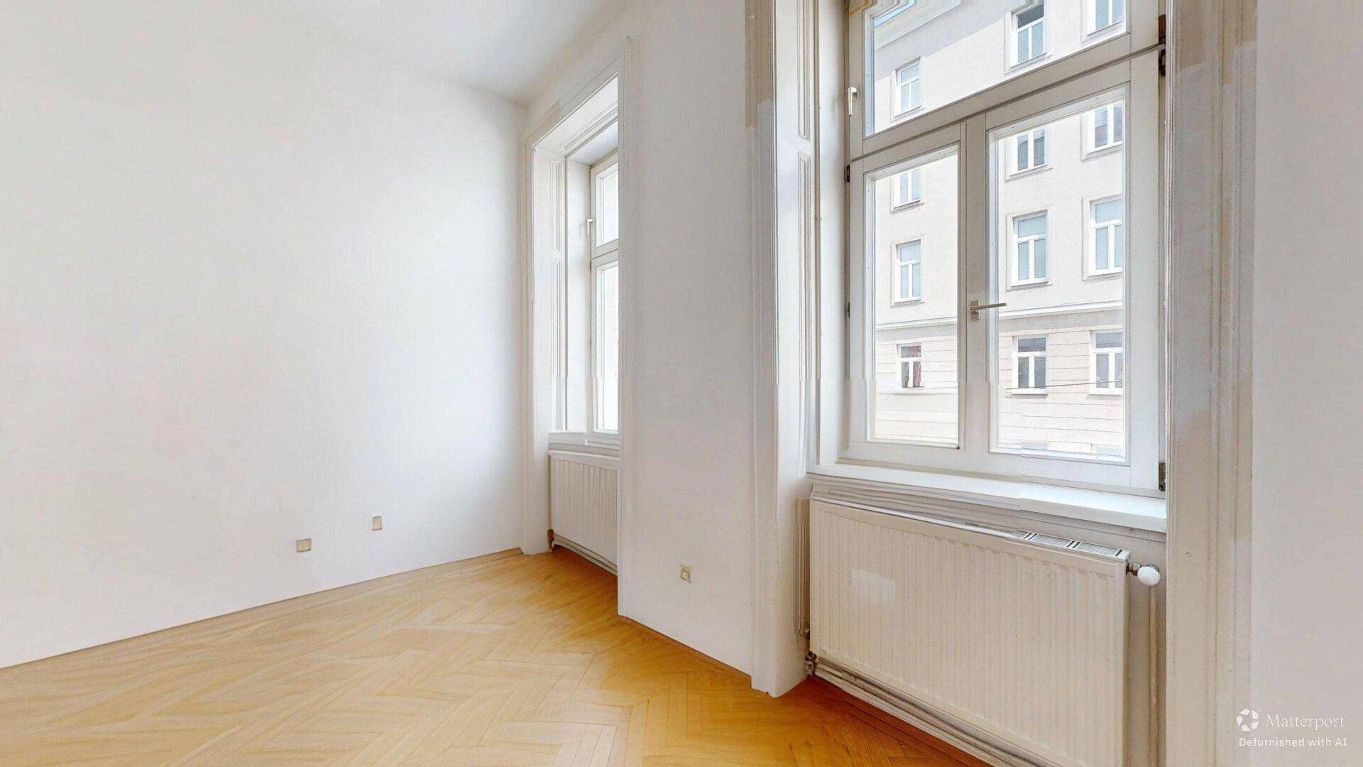 Lichtdurchflutetes Zimmer mit Fischgrätparkett und hohen Fenstern, bietet viel Tageslicht.