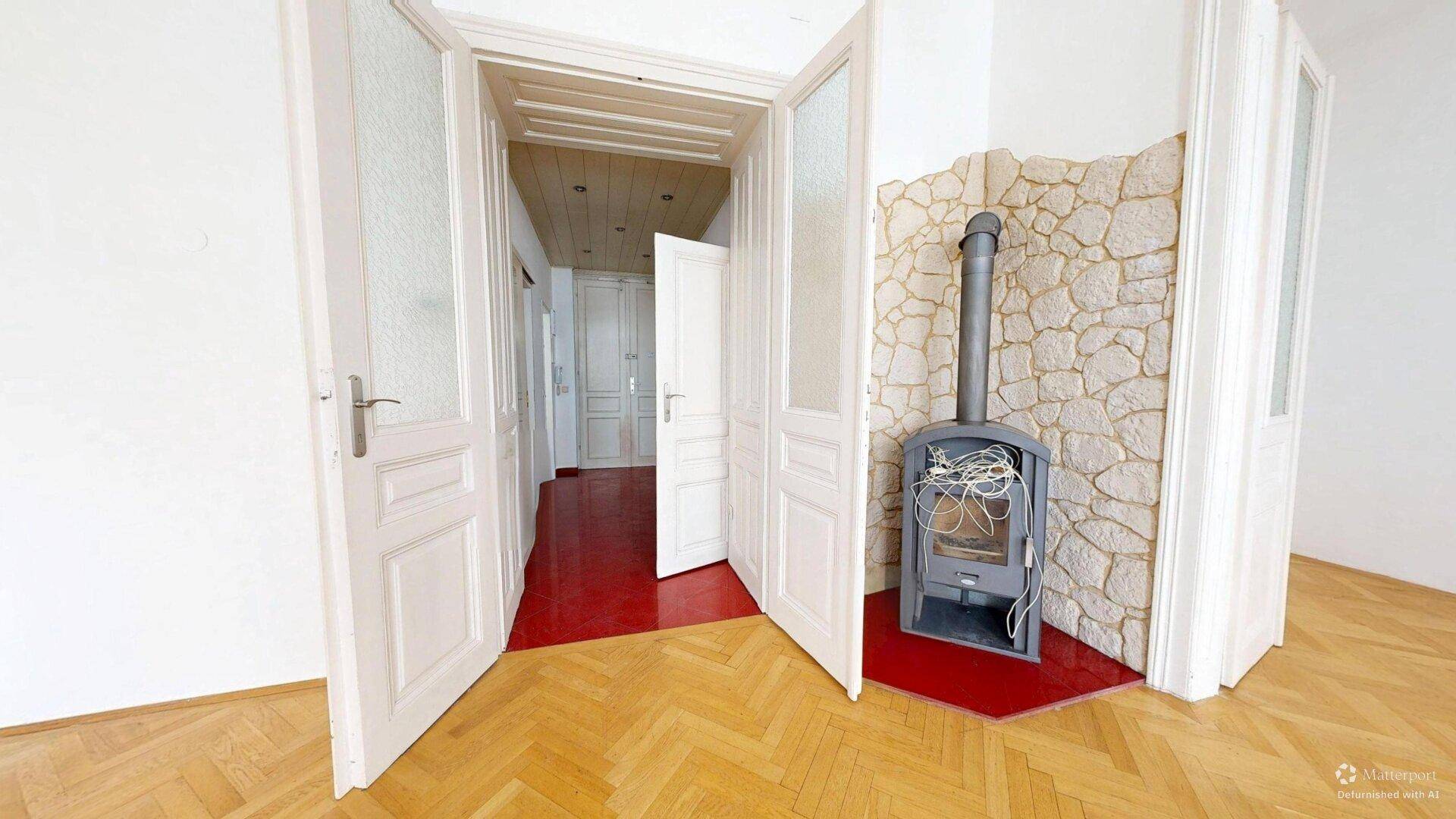 Helles Zimmer mit Fischgrätparkett, Holzofen und Zugang zu weiteren Räumen durch Flügeltüren.