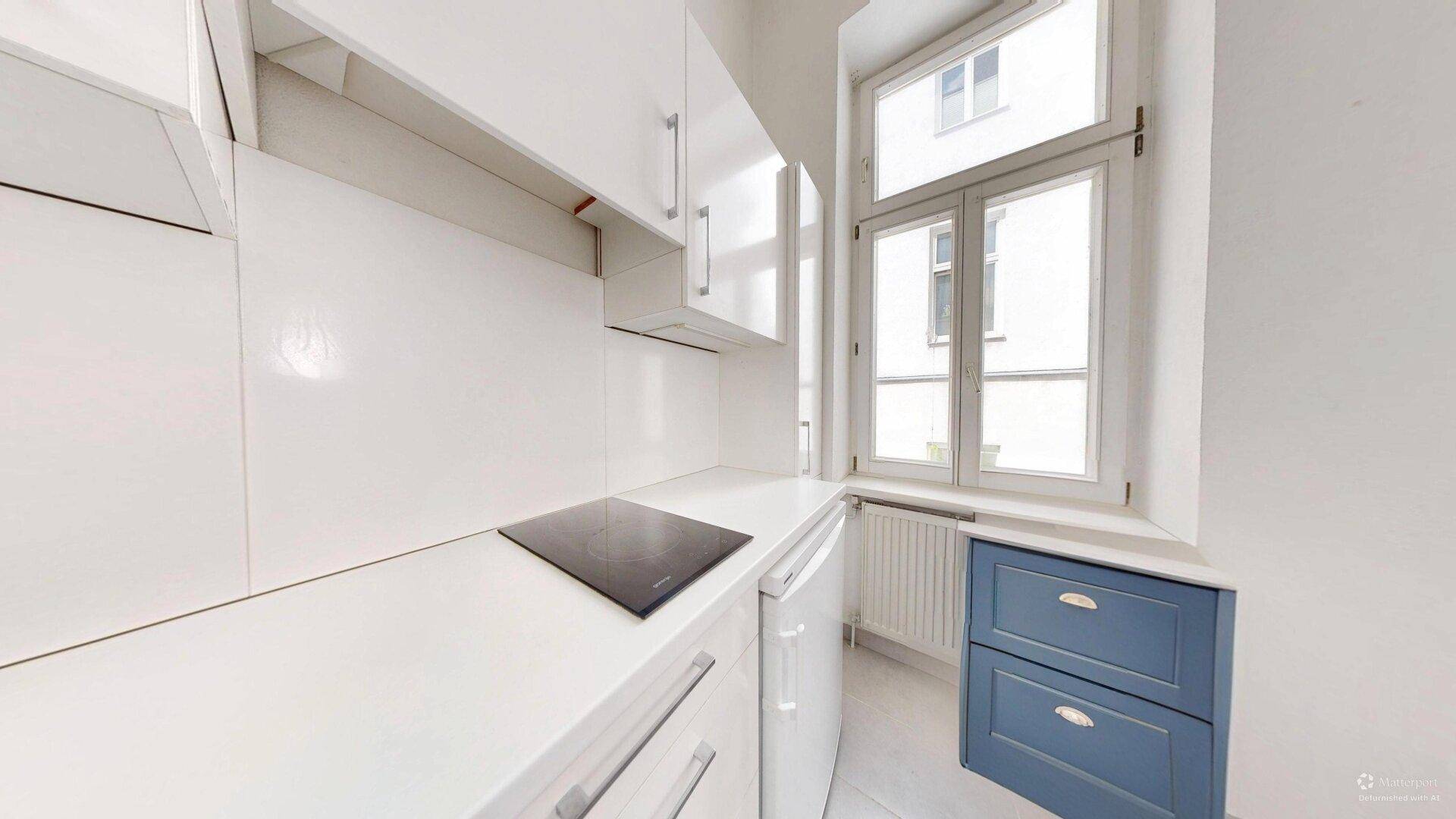 Moderne Küchenzeile mit Induktionskochfeld, weißen Schränken und einem Fenster, ergänzt durch blaue Schubladen.