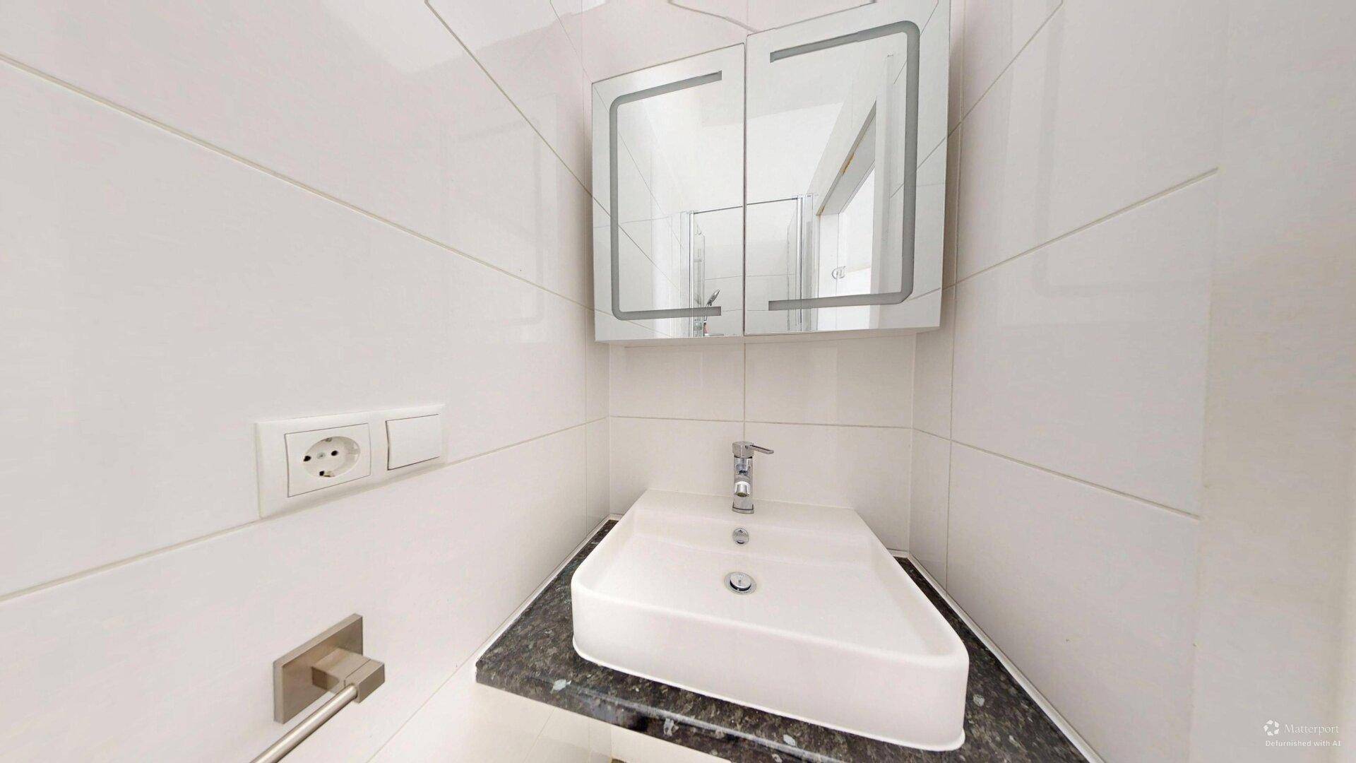 Modernes Badezimmer mit stilvollem Waschbecken, dunkler Arbeitsplatte und beleuchtetem Spiegelschrank.