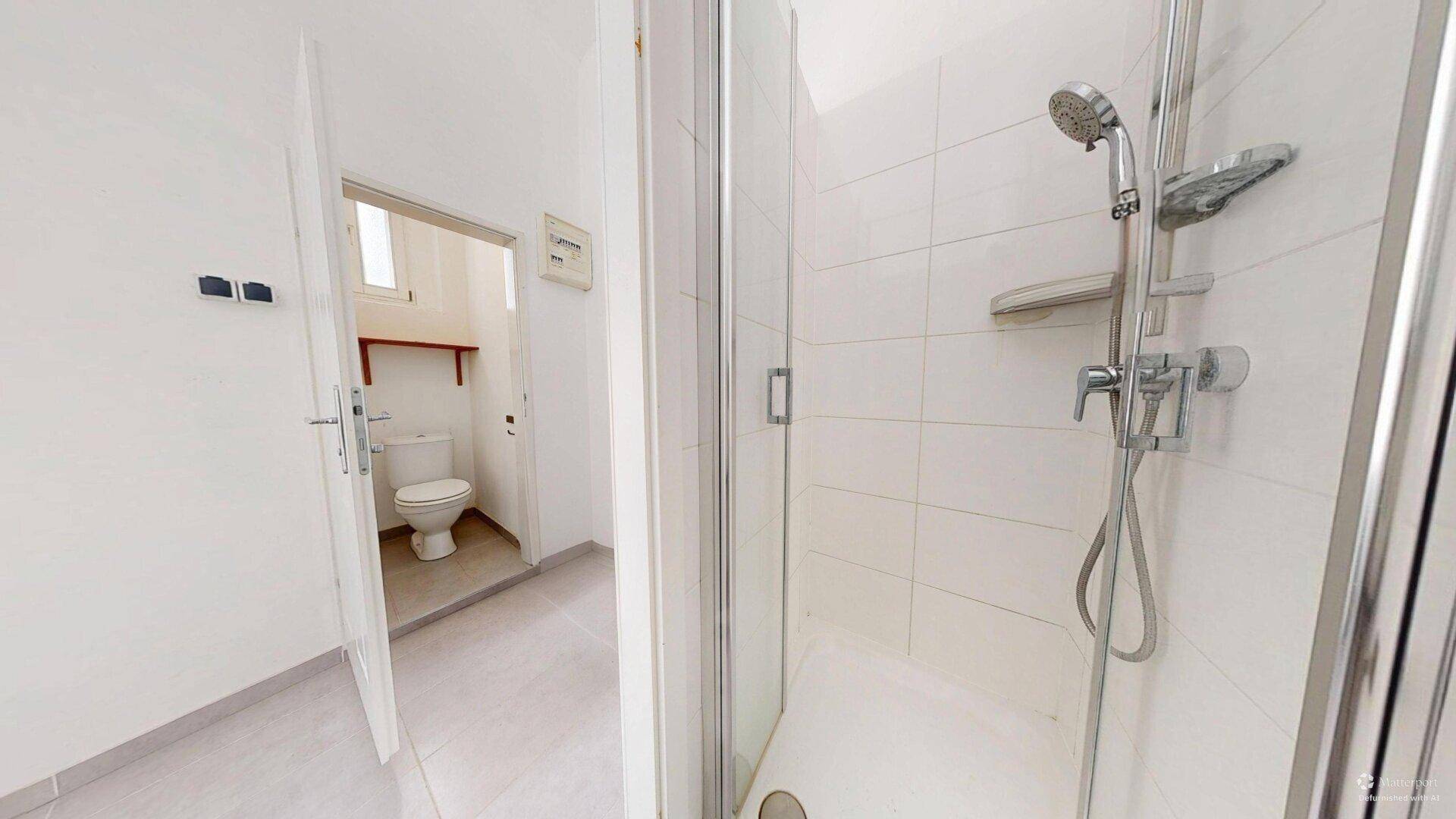 Duschbereich mit weiß gefliesten Wänden und Blick in einen separaten Toilettenraum.
