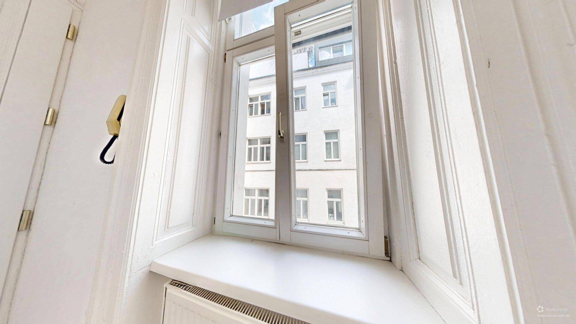 Fenster in einem hellen Raum mit Blick auf die Fassade eines gegenüberliegenden Gebäudes.