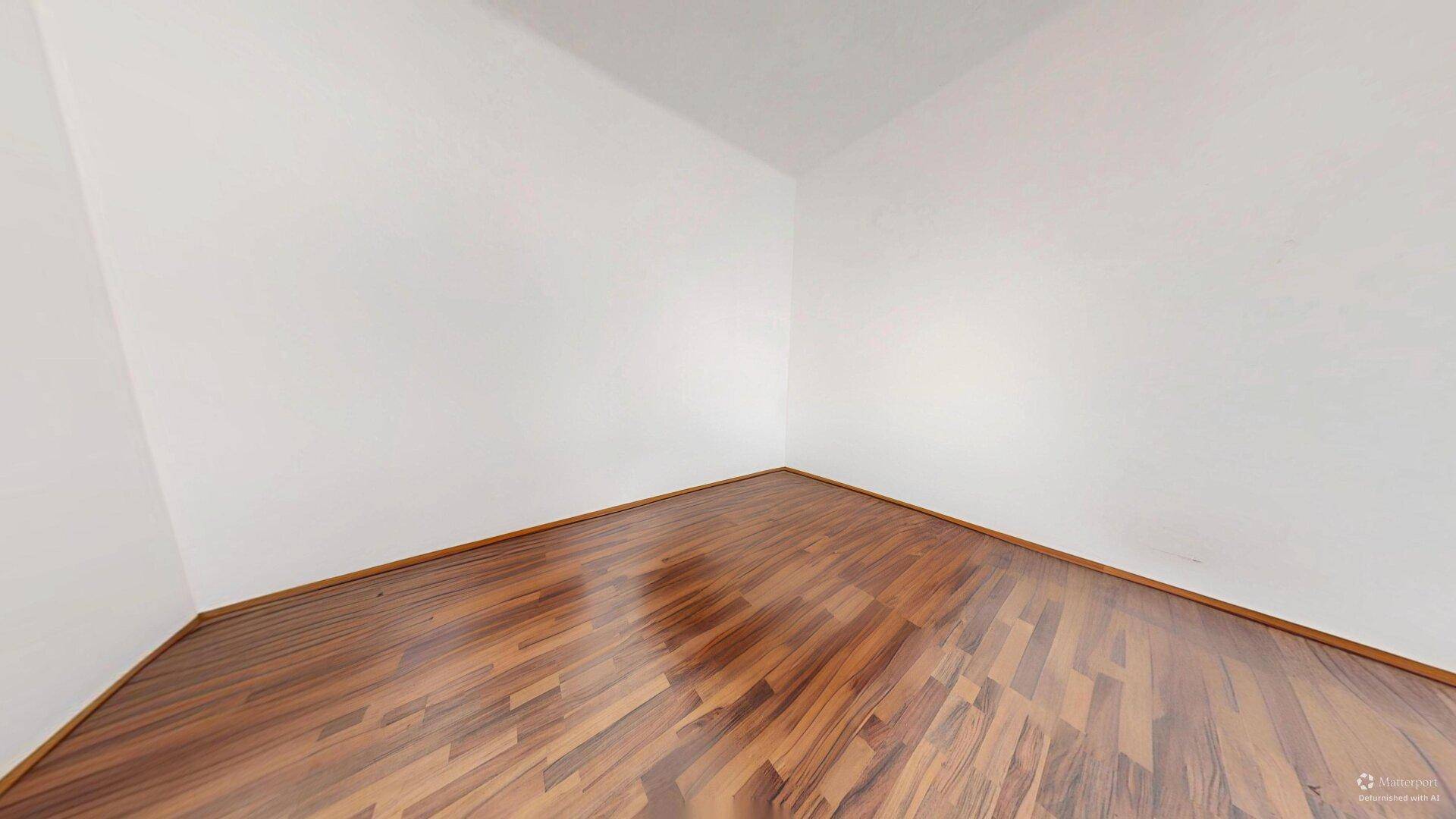 Leere Ecke eines Zimmers mit glänzendem Holzboden und sauberen weißen Wänden.