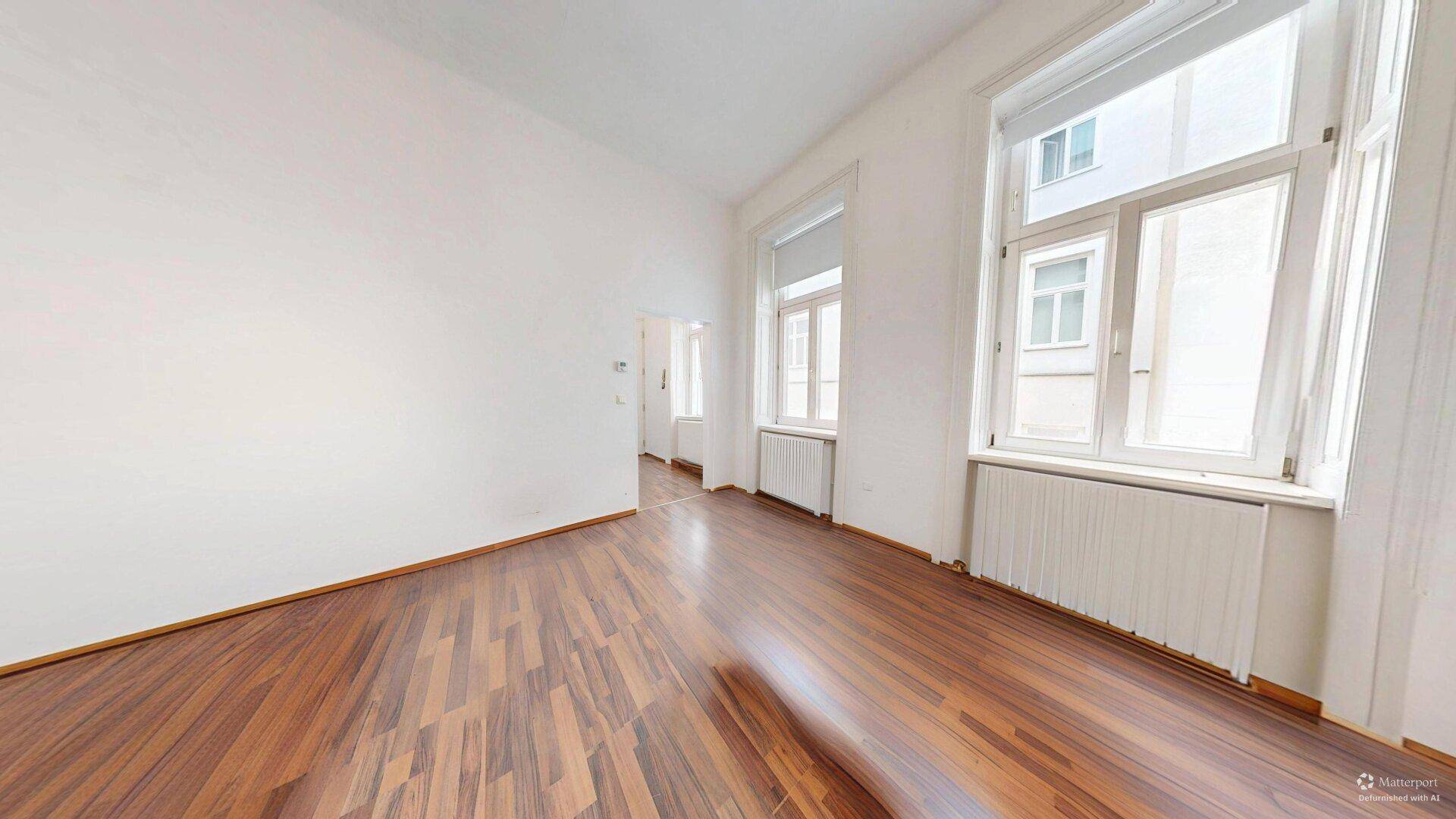 Helles Zimmer mit zwei Fenstern, Holzboden und weißen Wänden, ideal als Wohnbereich nutzbar.
