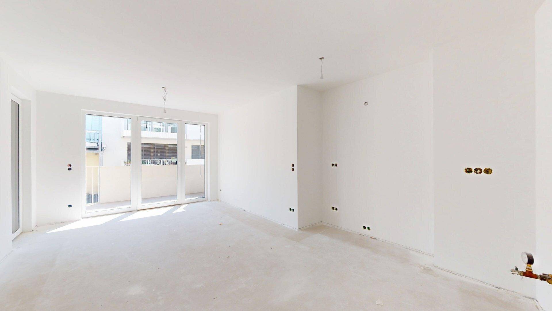 Rohbau-Wohnbereich mit vorbereiteten Installationen und Zugang zu einem Balkon, ideal für individuelle Gestaltung.