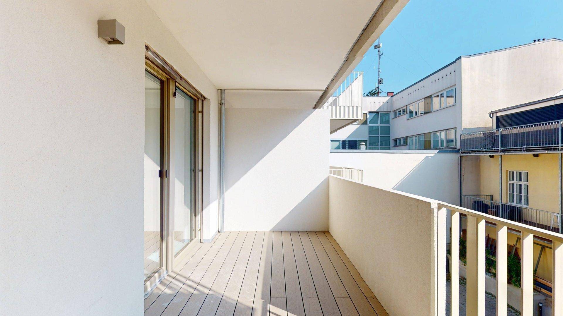 Geräumiger Balkon mit Holzboden und weißem Geländer, bietet einen Blick auf die umliegenden Gebäude.