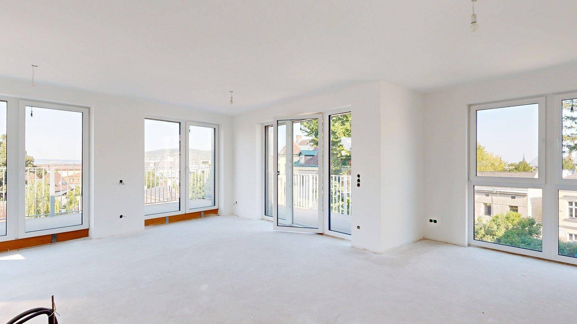 Geräumiger, heller Raum im Neubau mit mehreren Fenstern und Zugang zu Außenbereichen, ideal für offenes Wohnen.