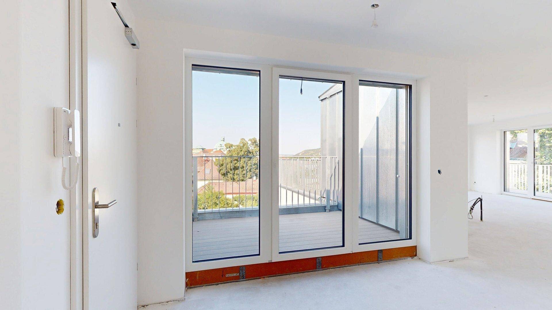 Heller Eingangsbereich mit Gegensprechanlage und großem Fenster, das Zugang zu einer Terrasse bietet.