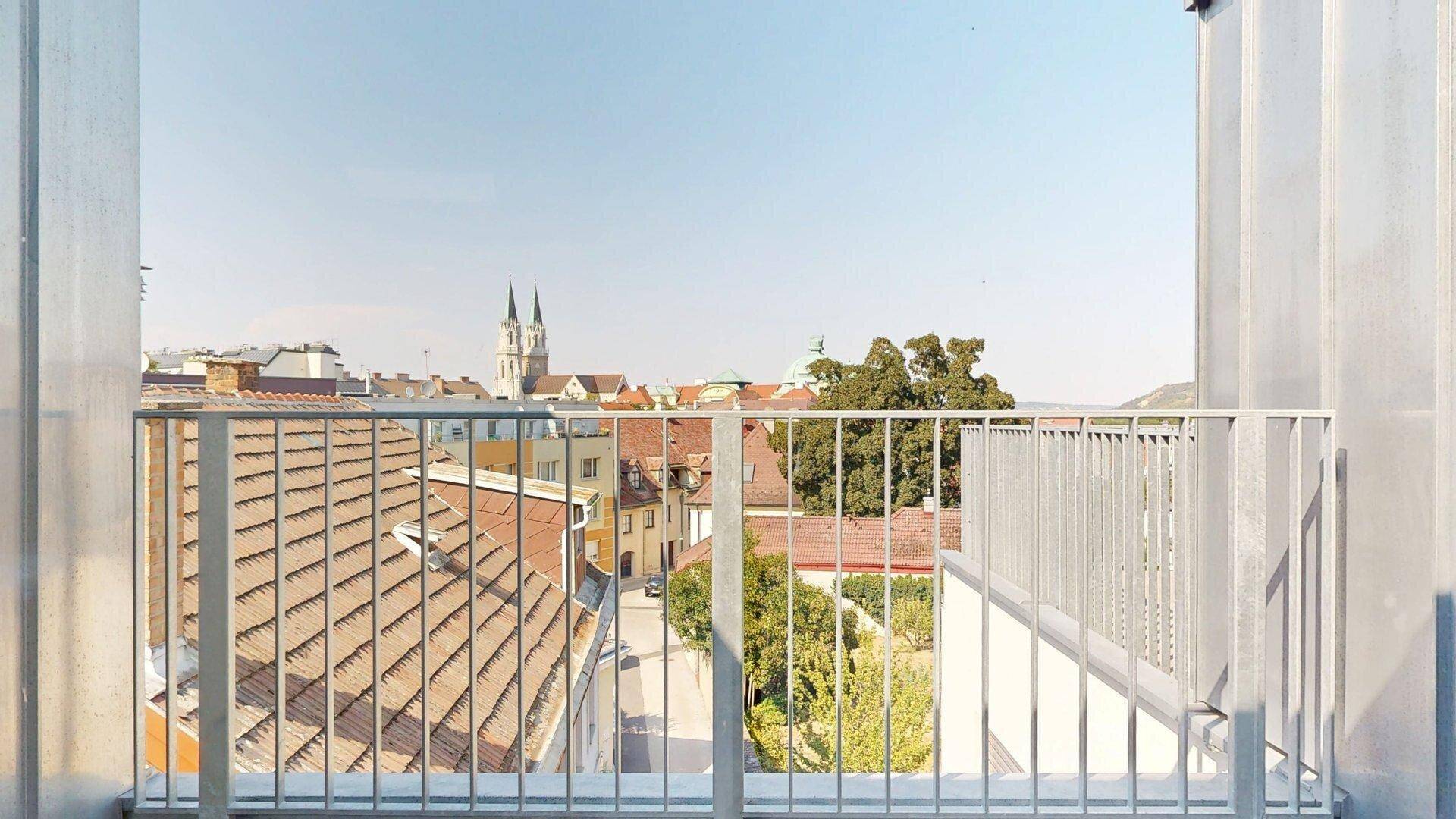 Panoramablick vom Balkon über die Dächer der Stadt mit historischer Kirche im Hintergrund.