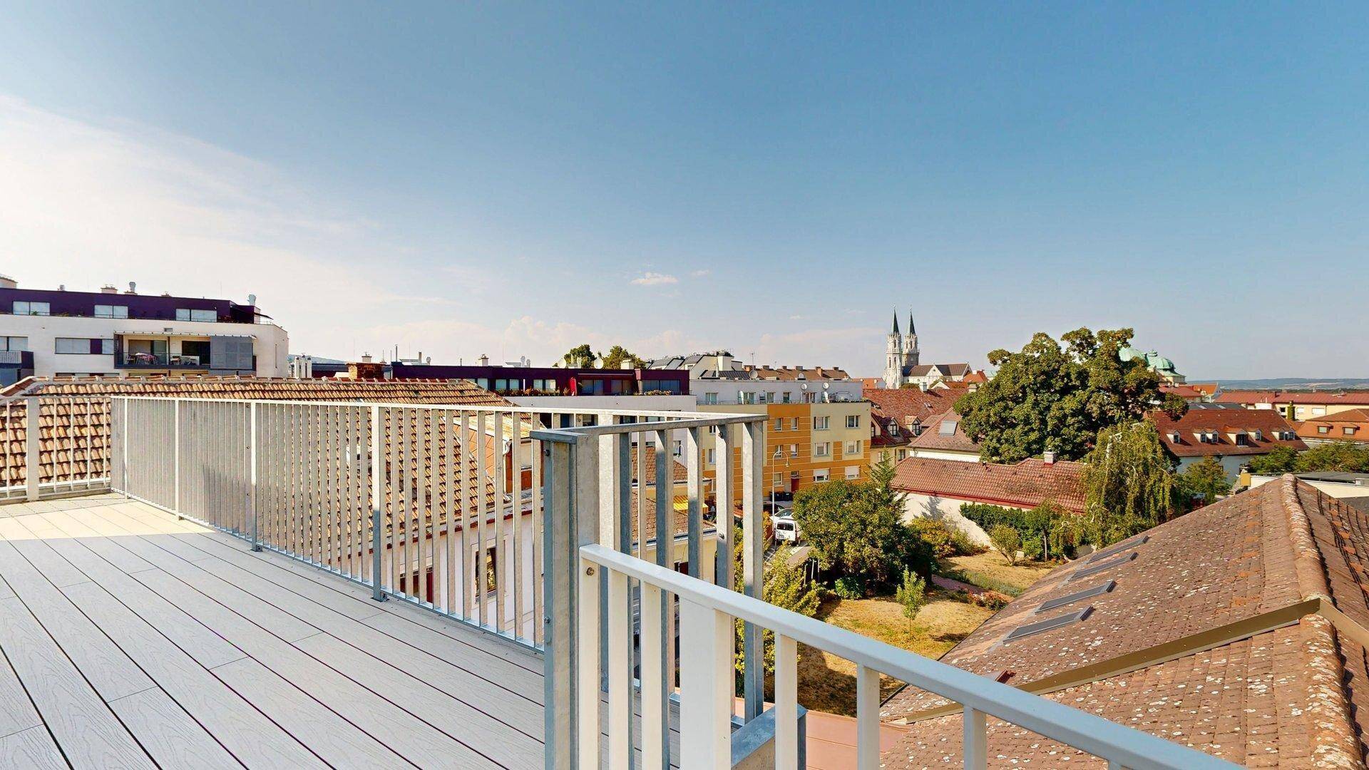Weitläufige Dachterrasse mit Holzboden und Panoramablick über die Stadt und historische Gebäude.