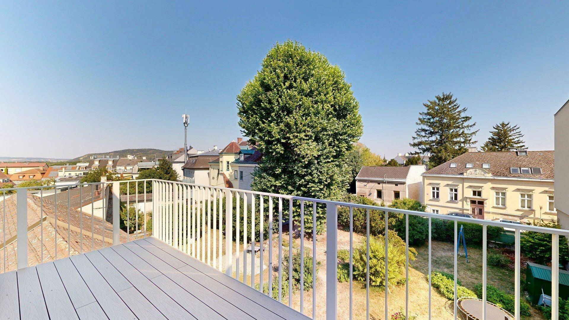 Geräumige Terrasse mit Holzboden und Blick auf einen großen Baum sowie die umliegende Wohngegend.