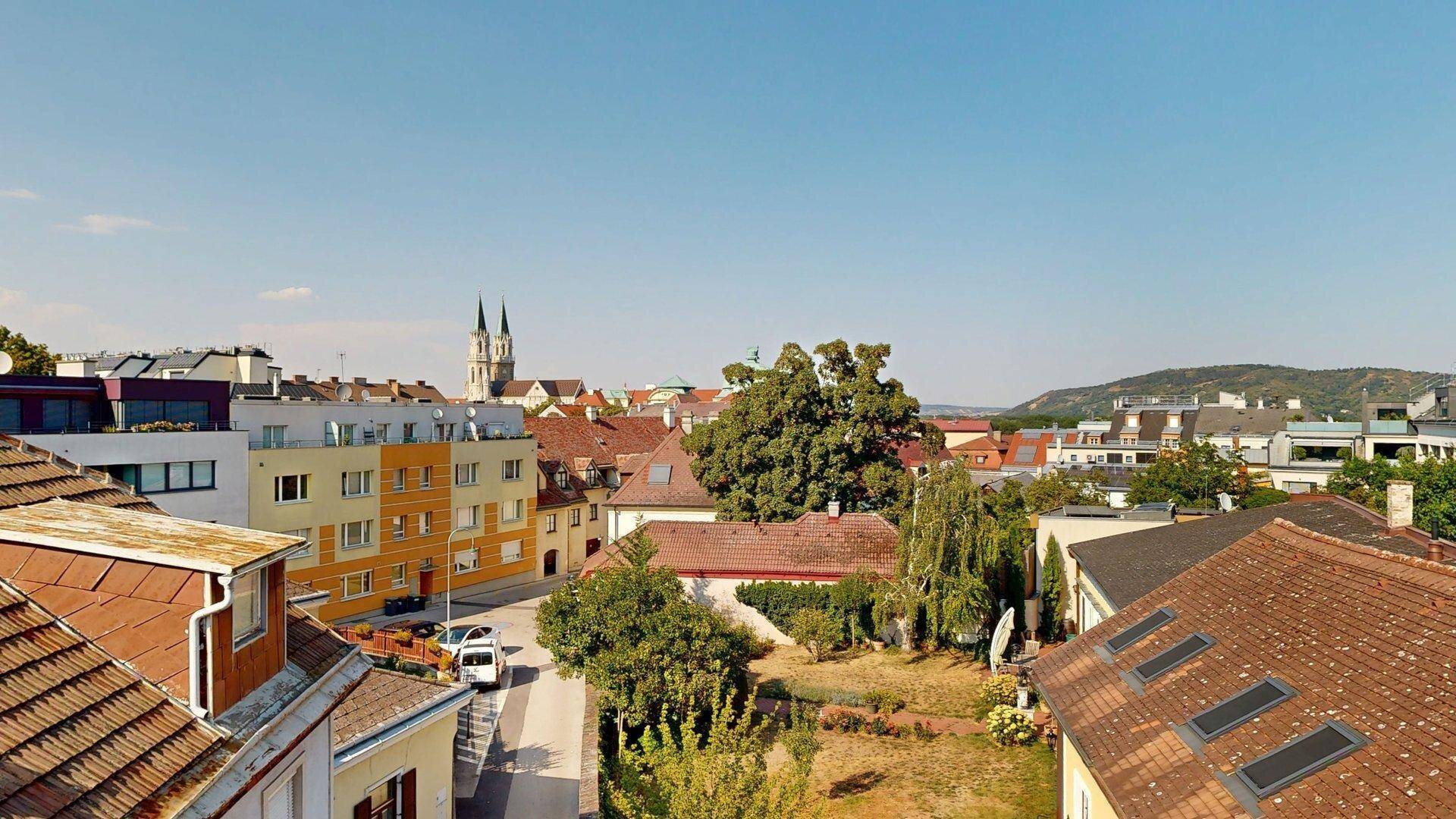 Überblick über die Wohngegend mit Dächern, Bäumen und einer Kirche im Hintergrund unter blauem Himmel.