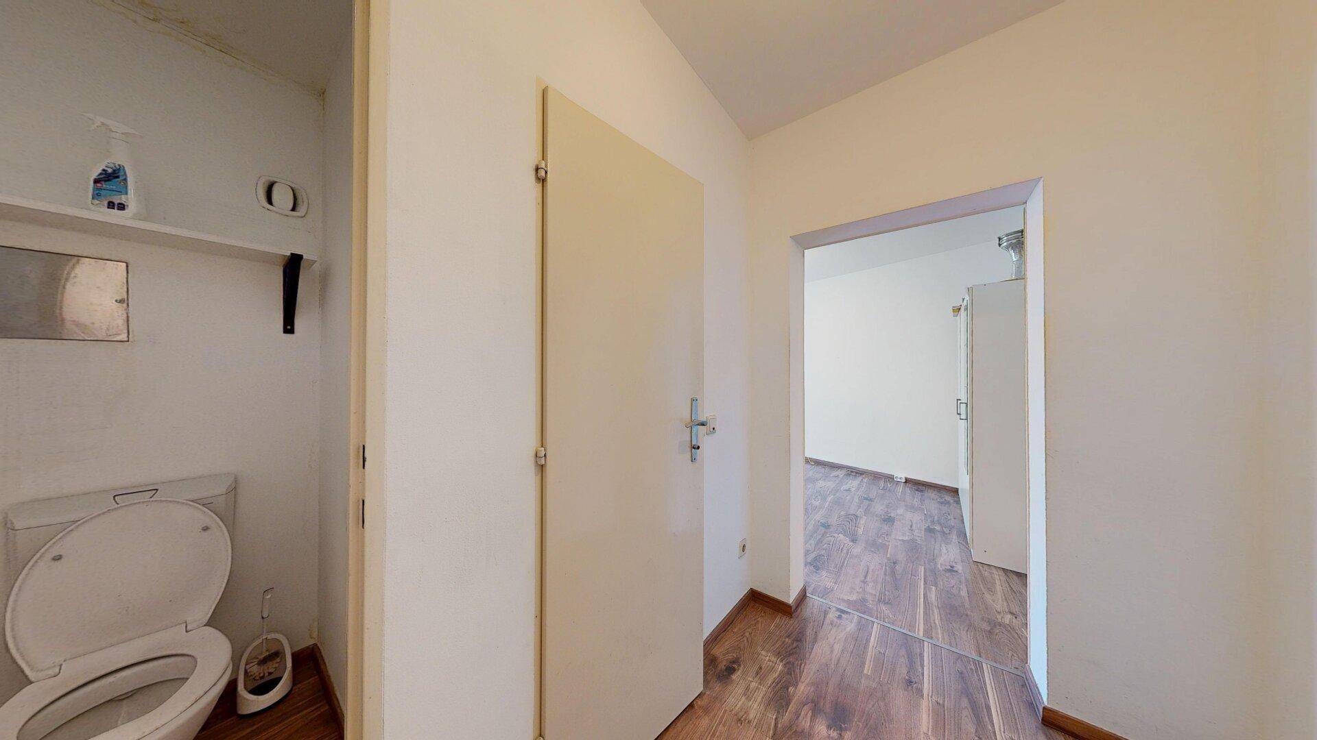 Kleines separates WC mit Toilette und einfacher Ausstattung, angrenzend an einen weiteren Raum.