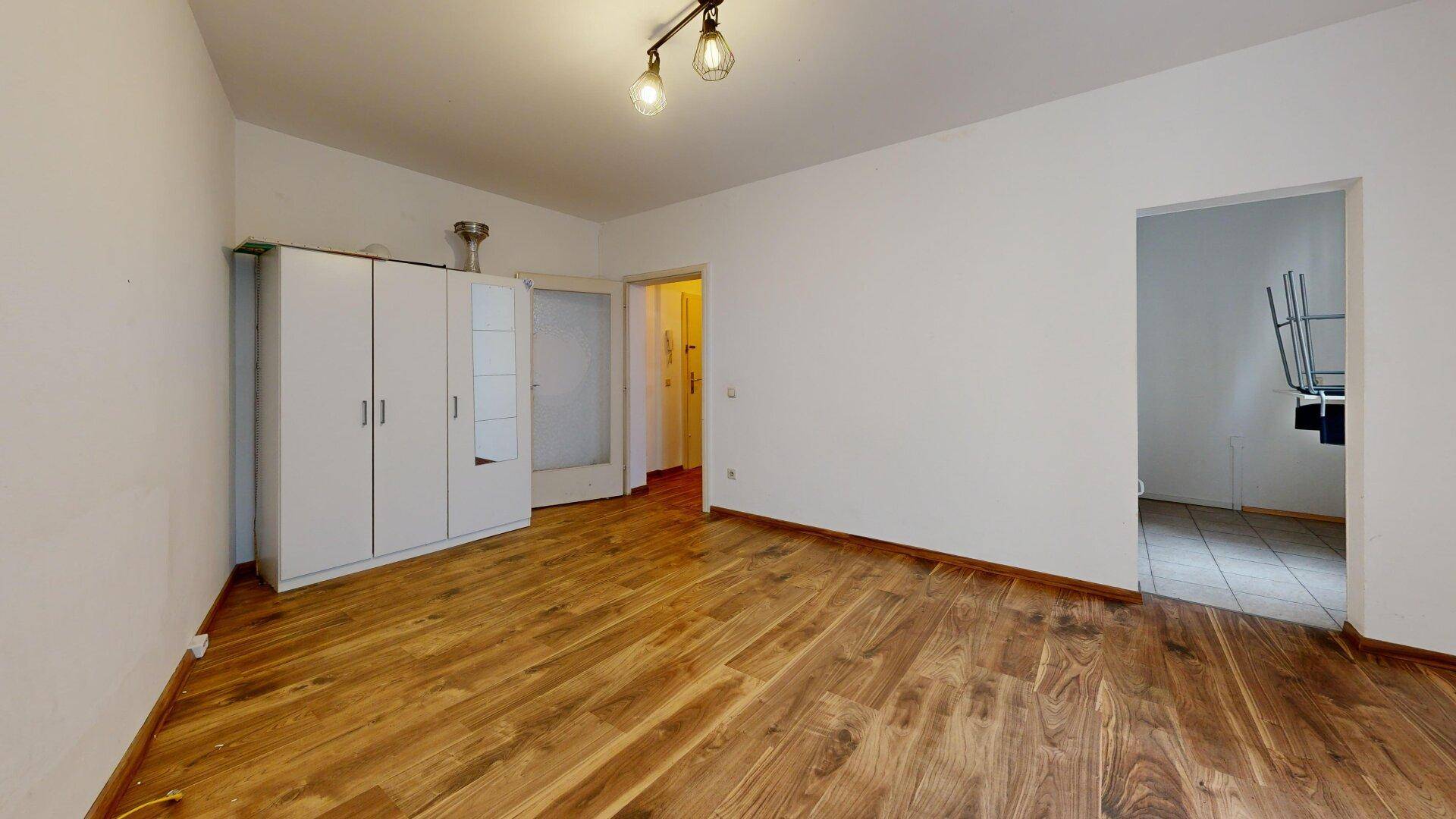Geräumiger Wohnbereich mit Holzboden, weißen Wänden und einem praktischen Kleiderschrank.