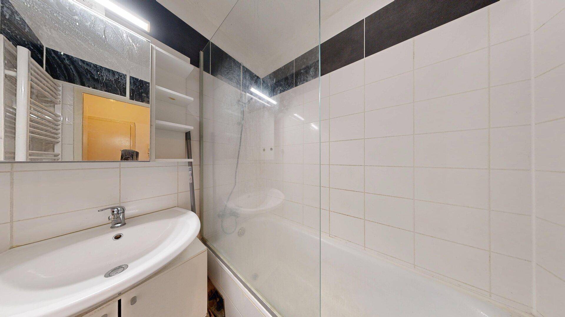 Modernes Badezimmer mit Badewanne, Duschwand, Waschbecken und weiß-schwarzen Fliesen.