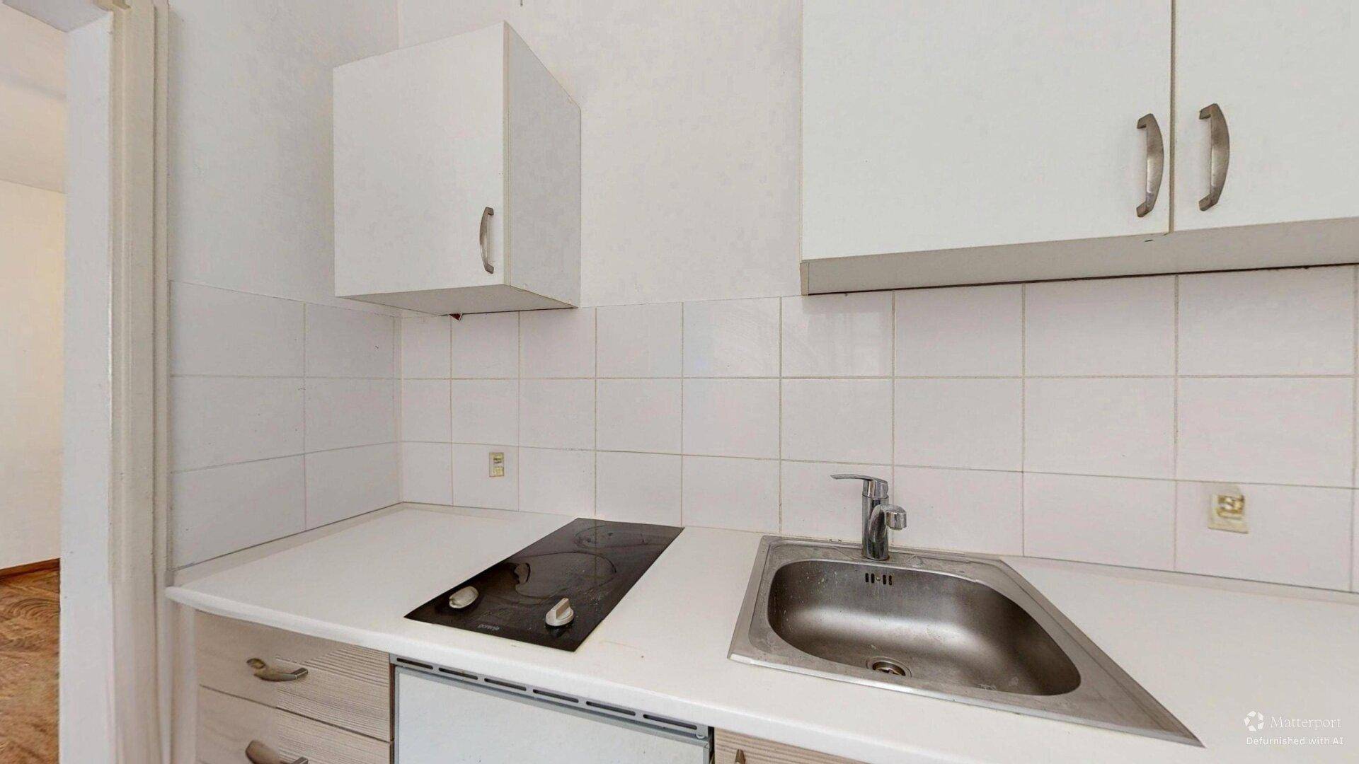 Kompakte Küchenzeile mit weißen Schränken, Spüle und zwei Kochfeldern, ideal für kleine Haushalte.