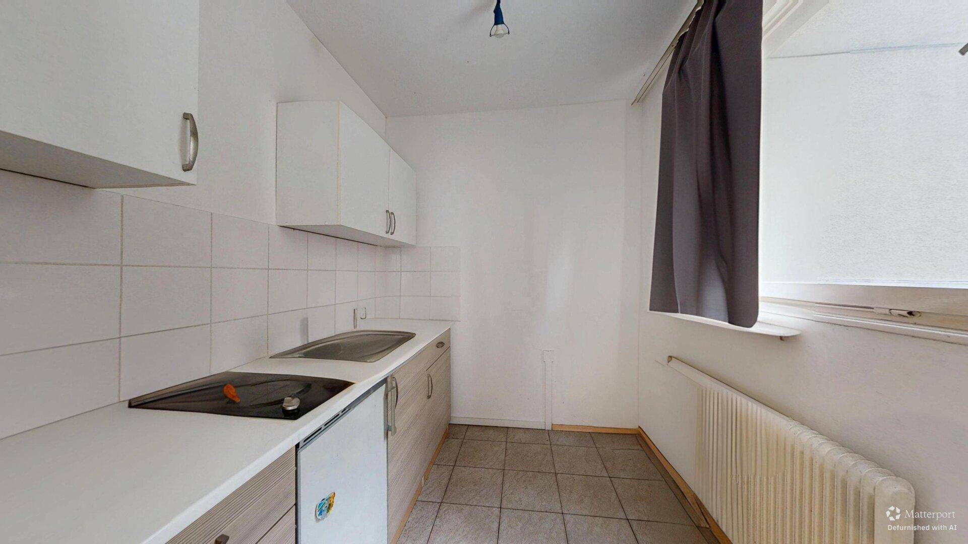 Funktionale Küchenzeile mit weißen Schränken, Spüle, Kochfeld und Fenster mit Vorhang.