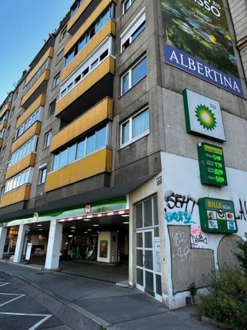 Mehrstöckiges Gebäude mit gelben Balkonen und einer Tankstelle im Erdgeschoss in urbaner Umgebung.