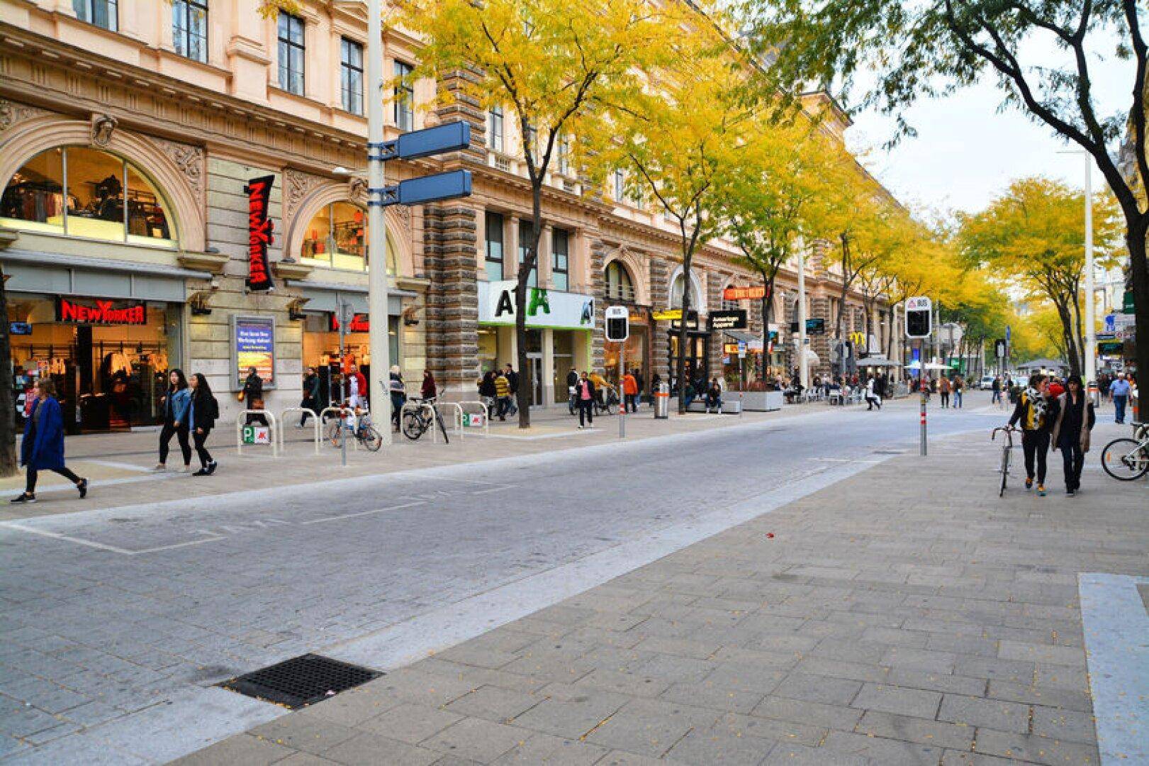 Belebtes Stadtbild mit Geschäften, Fußgängern und Bäumen mit herbstlichem Laub.