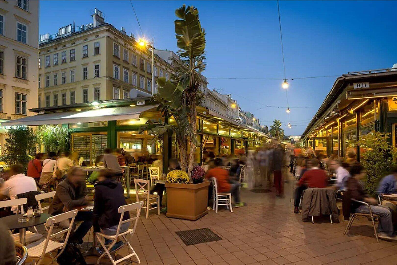 Beleuchtete Marktstraße am Abend mit zahlreichen Restaurants, Außensitzplätzen und Passanten.