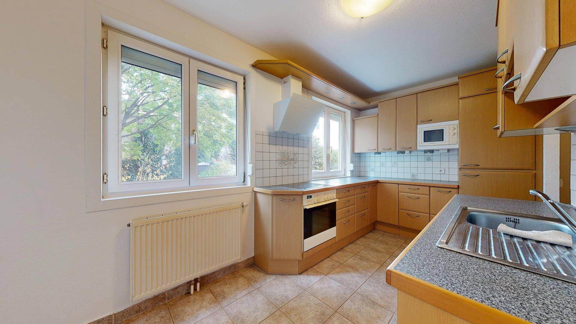 Helle Küche mit Holzfronten, Fliesenboden, Fenster und modernen Einbaugeräten.