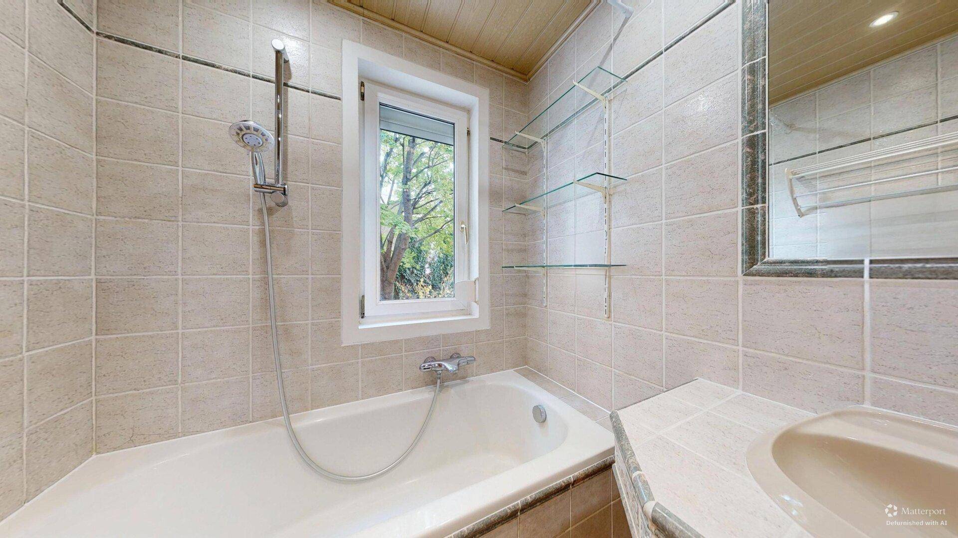 Badezimmer mit beigefarbenen Fliesen, Badewanne mit Duschfunktion und Fenster für Tageslicht.