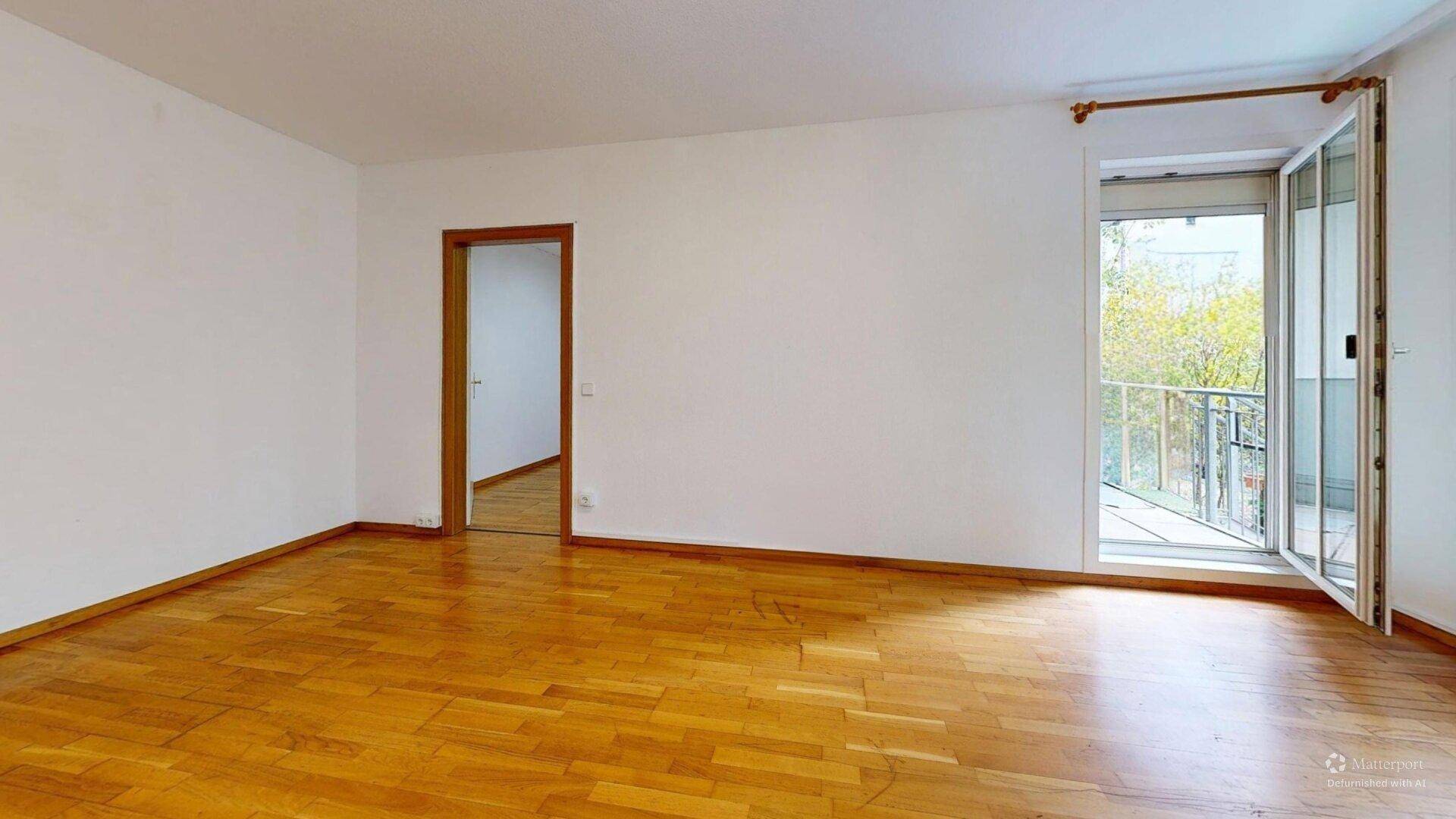 Geräumiges Zimmer mit Parkettboden, weißen Wänden und großem Balkonzugang für viel Licht.