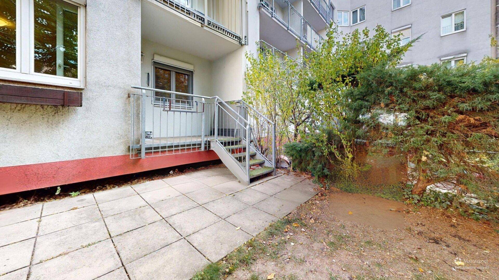 Gepflasterte Terrasse mit Treppenzugang zu einem oberen Bereich und angrenzendem Grünstreifen.