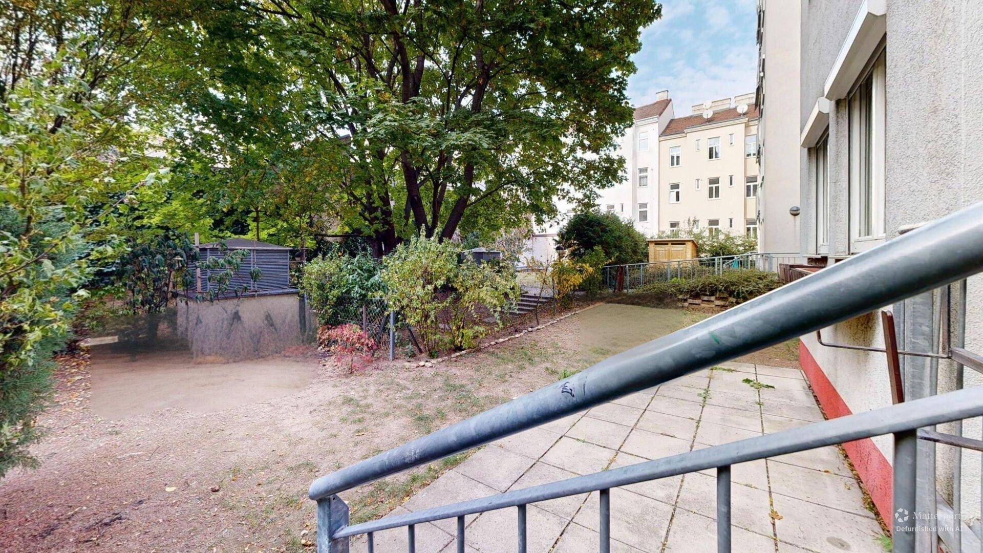 Außenbereich mit gepflastertem Weg, Treppe und einem naturbelassenen Gartenabschnitt neben dem Gebäude.