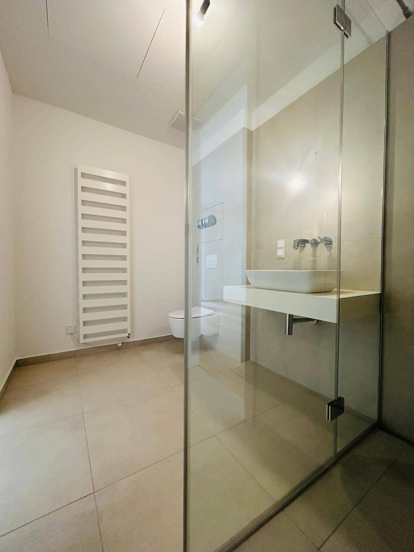 Helles Badezimmer mit moderner Dusche, WC und beheiztem Handtuchhalter.