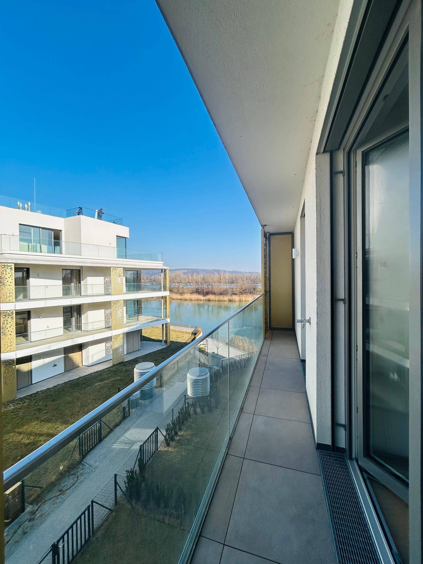 Geräumiger Balkon mit Glasgeländer und weitem Blick auf den See.