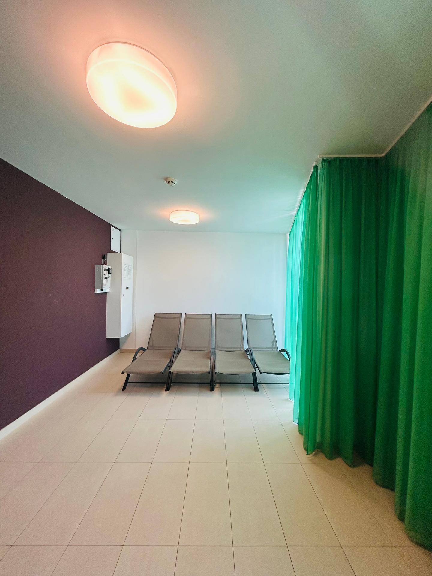 Entspannungsbereich mit Liegestühlen und grünen Vorhängen in einem Gemeinschafts-Wellnessbereich.