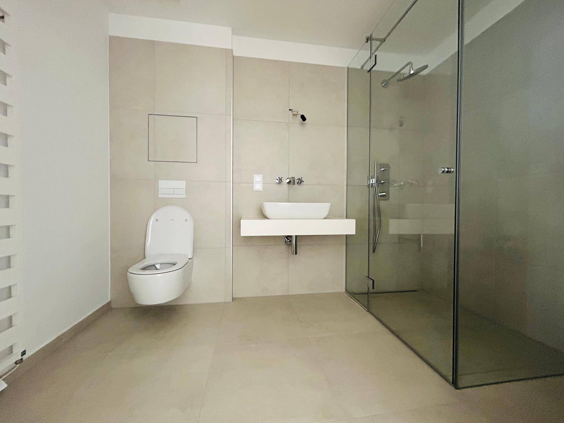 Modernes Badezimmer mit wandhängendem WC, Einzelwaschbecken und großer Glasdusche.