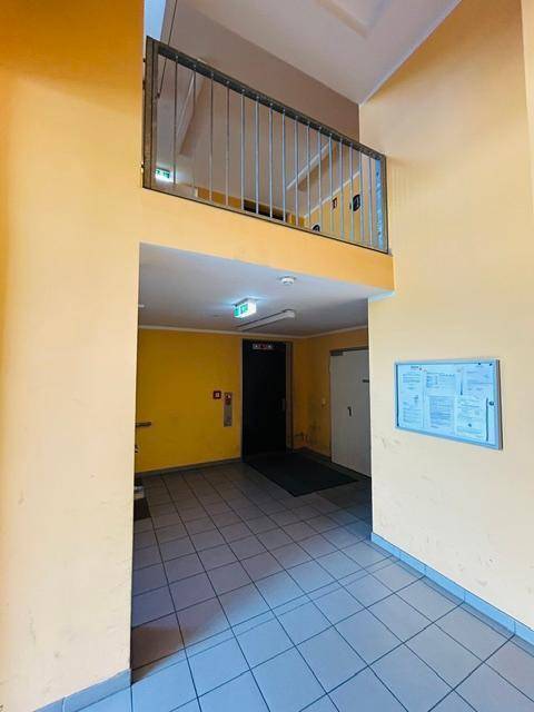 Treppenhaus und Flur in einem Wohngebäude mit gelben Wänden und Fliesenboden.