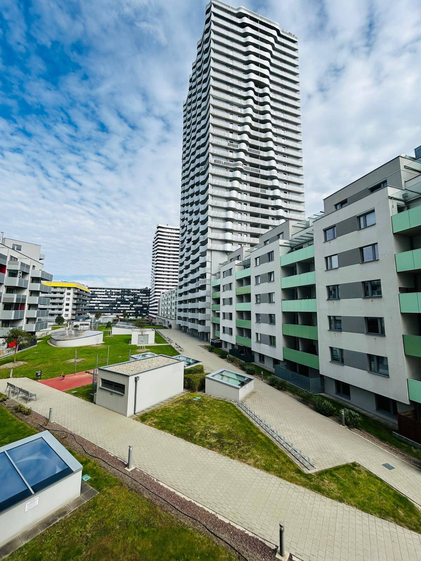 Moderne Wohnanlage mit Grünflächen und hohen Gebäuden unter blauem Himmel.