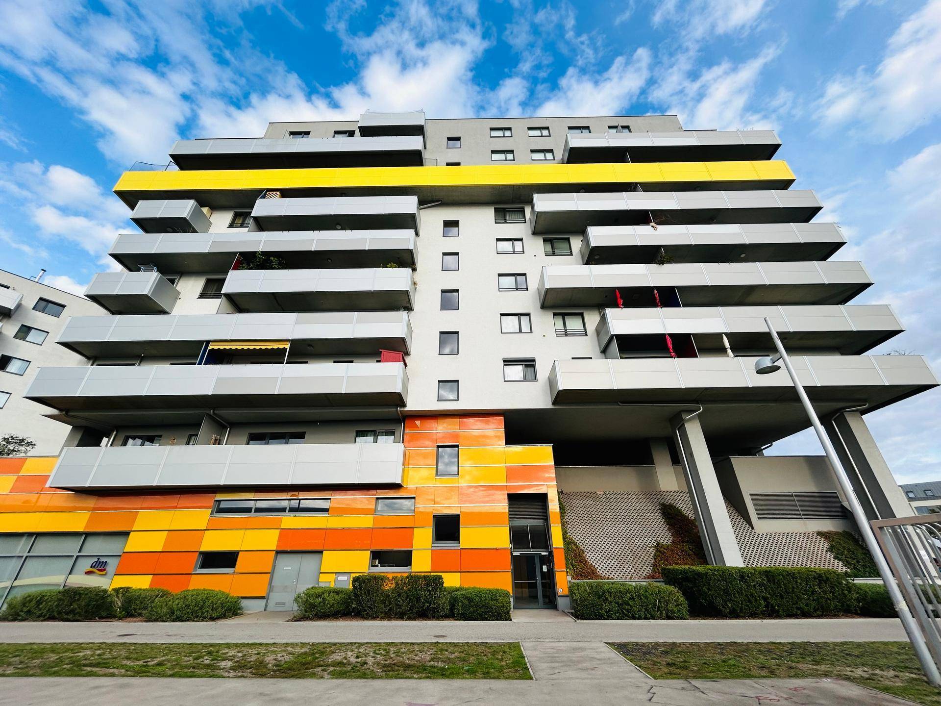 Bunte Fassade eines modernen Wohngebäudes mit Balkonen und Geschäften im Erdgeschoss.