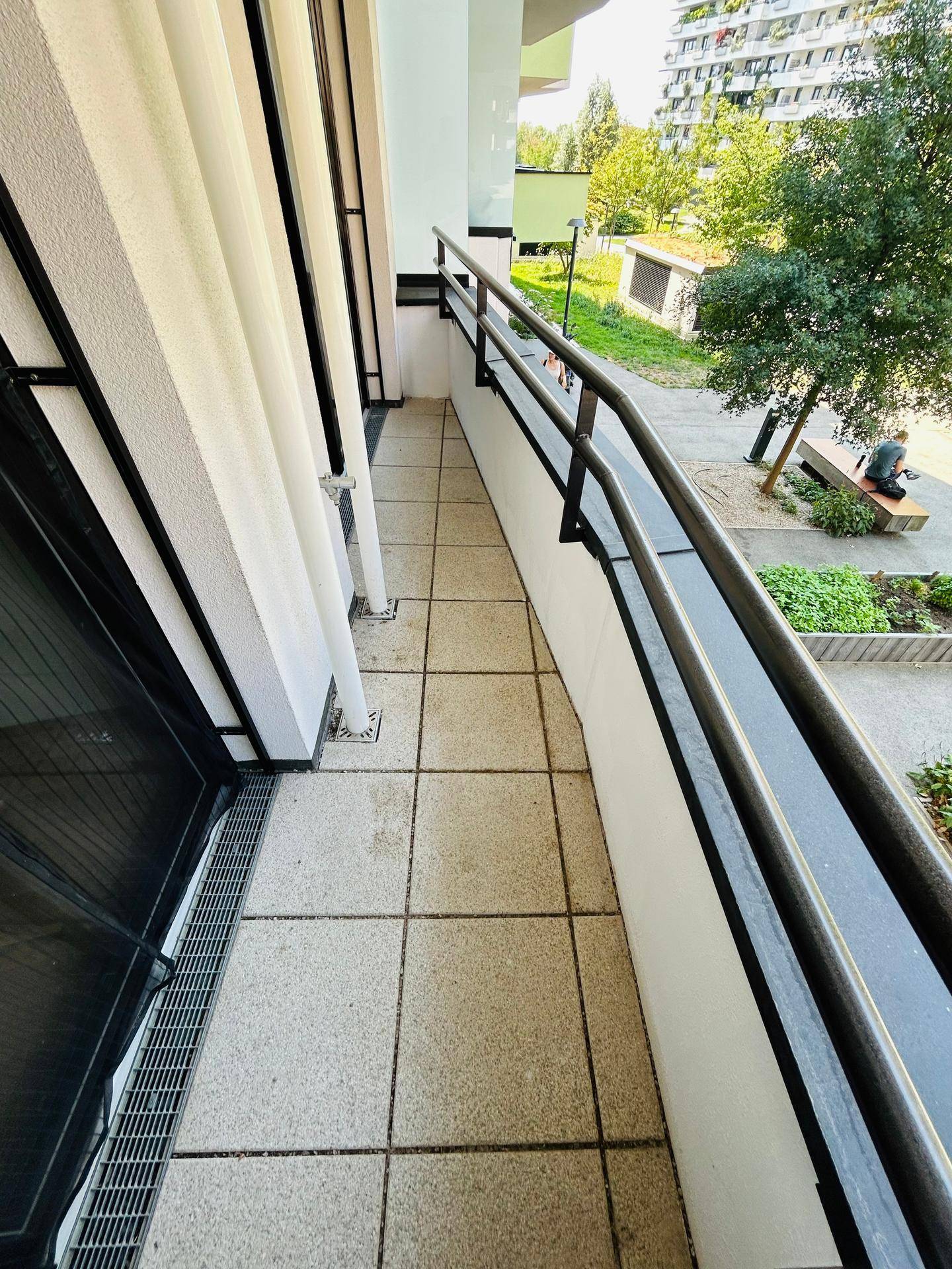 Gefliester Balkon mit Metallgeländer und Blick auf den begrünten Außenbereich der Wohnanlage.