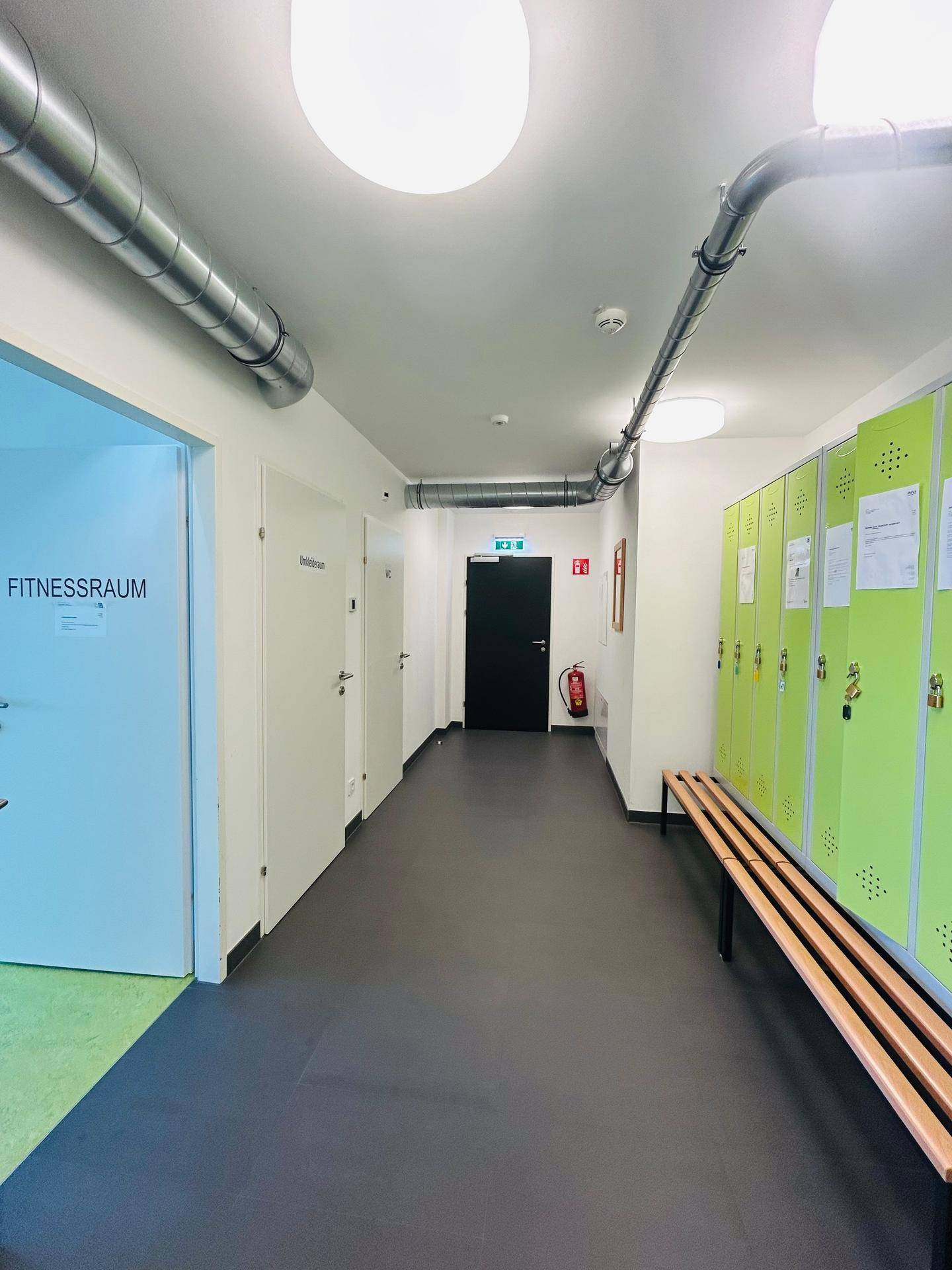 Flur im Gemeinschaftsbereich mit Spinden und Zugang zum Fitnessraum.