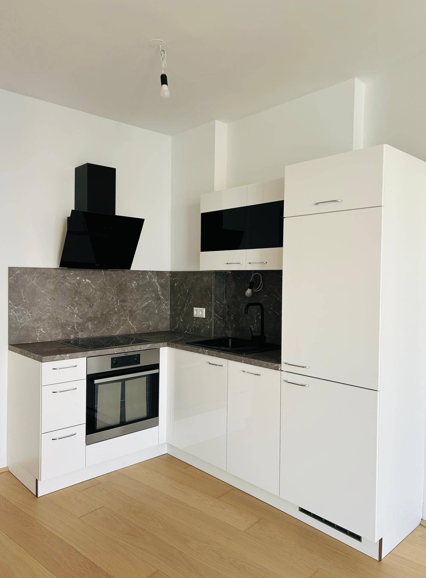 Moderne Einbauküche mit weißen Hochglanzfronten, dunkler Arbeitsplatte und integriertem Backofen.