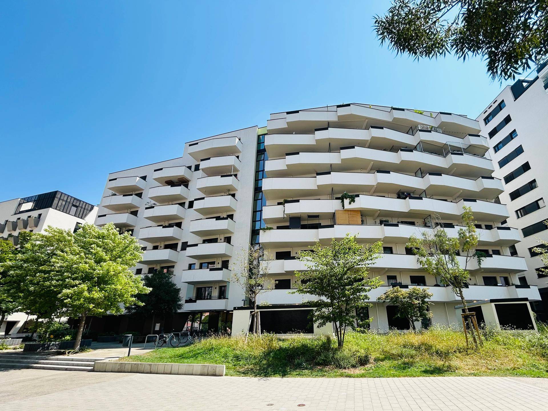 Moderne Wohnanlage mit markanten, geschwungenen Balkonen und gepflegten Grünflächen.