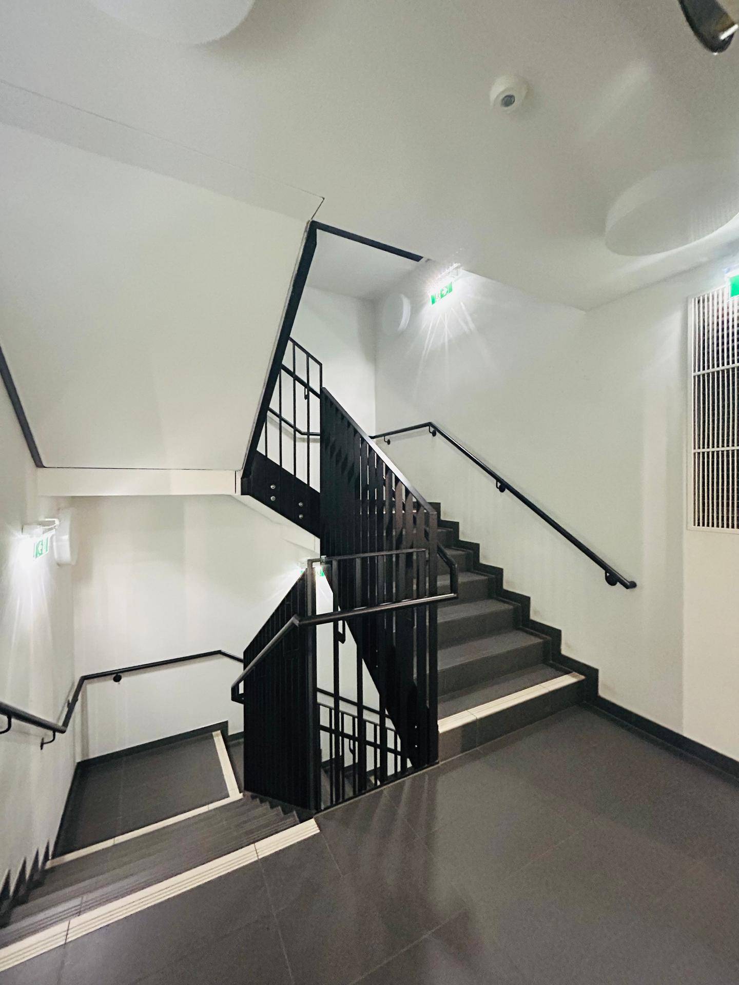 Modernes Treppenhaus mit dunklen Stufen und Metallgeländer, gut beleuchtet.