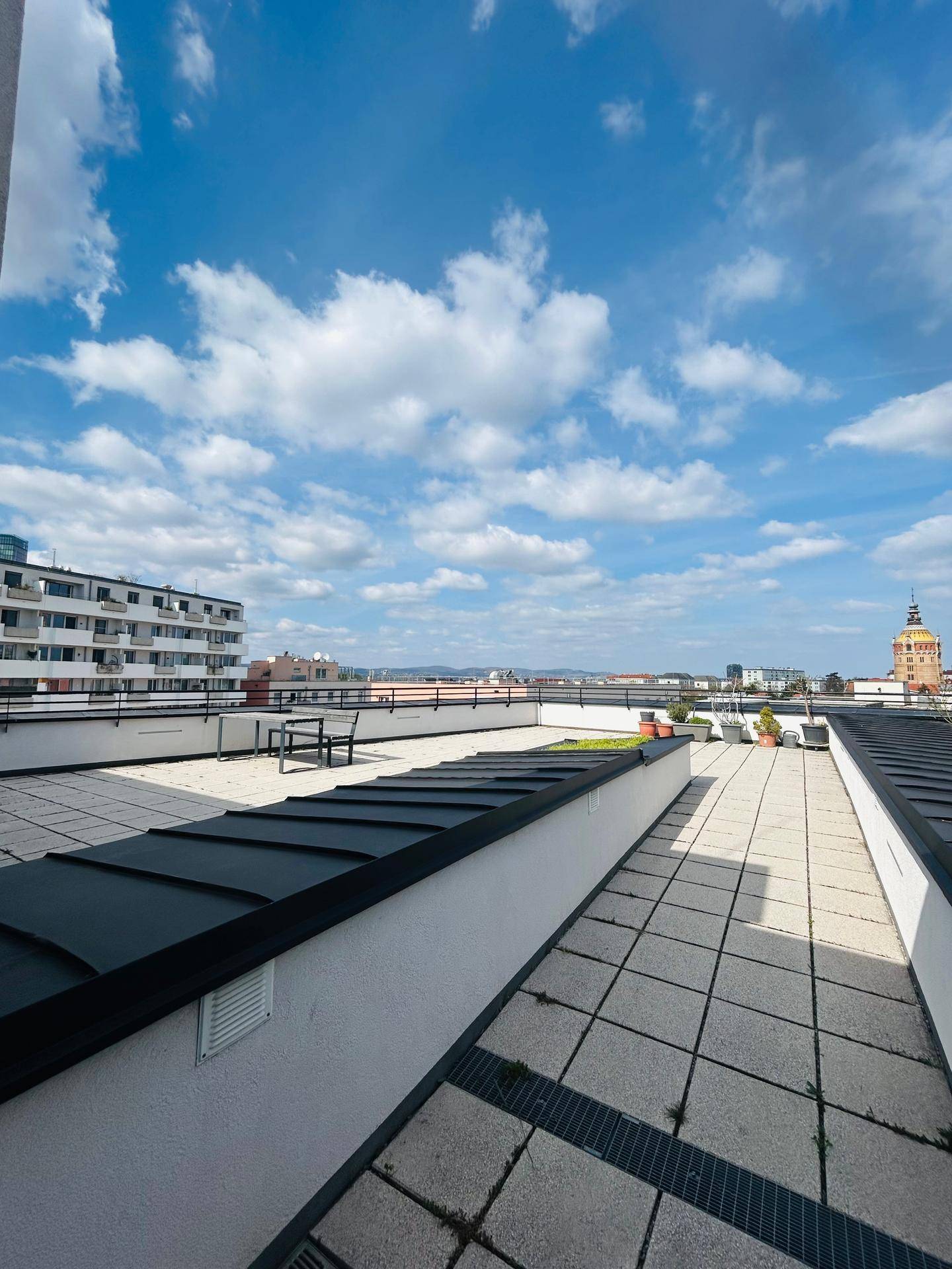 Weitläufige Dachterrasse mit Stadtblick und Sitzgelegenheiten unter blauem Himmel.