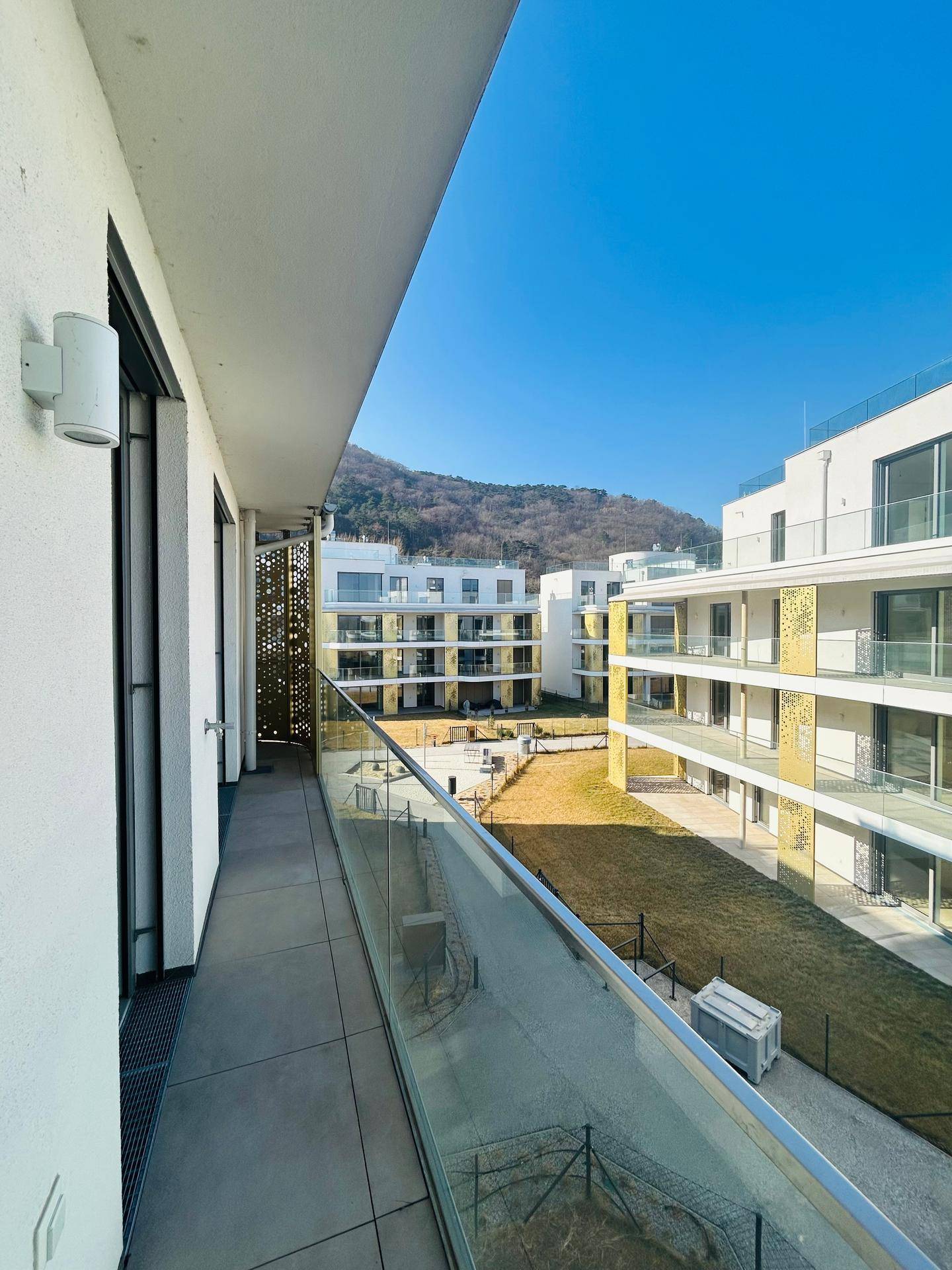 Langer Balkon mit Glasgeländer und Blick auf den Innenhof und die umliegenden Gebäude.