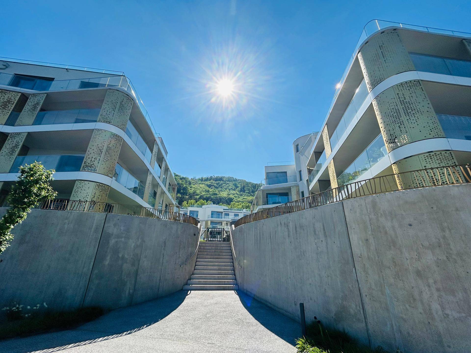 Moderne Wohngebäude mit geschwungenen Fassaden und Balkonen unter strahlend blauem Himmel mit Bergblick.