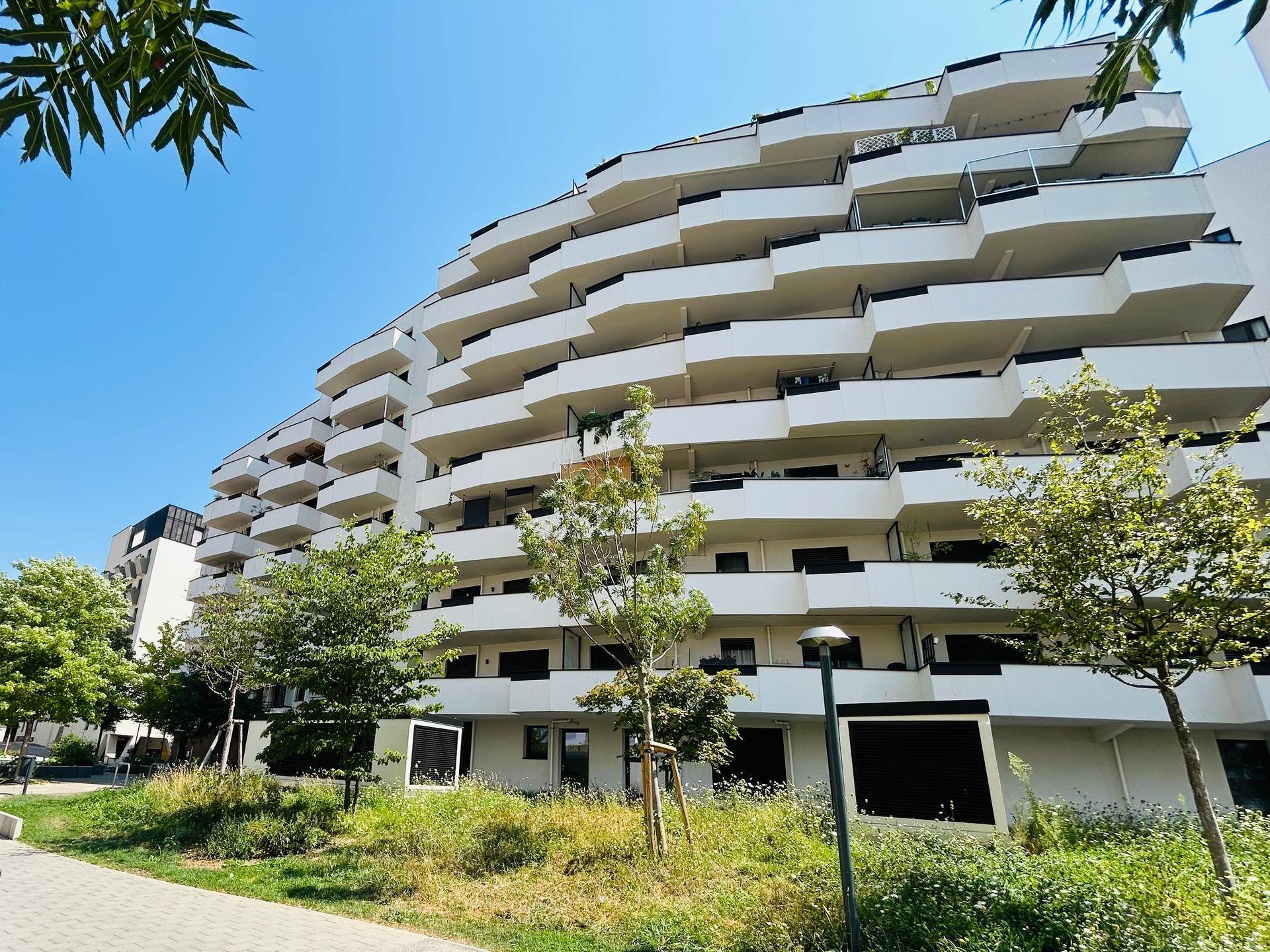 Moderne Architektur des Wohngebäudes mit geschwungenen Balkonen und viel Grün.